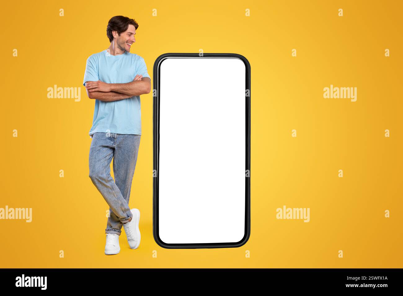 Guy standing near big empty smartphone screen with crossed hands Stock Photo