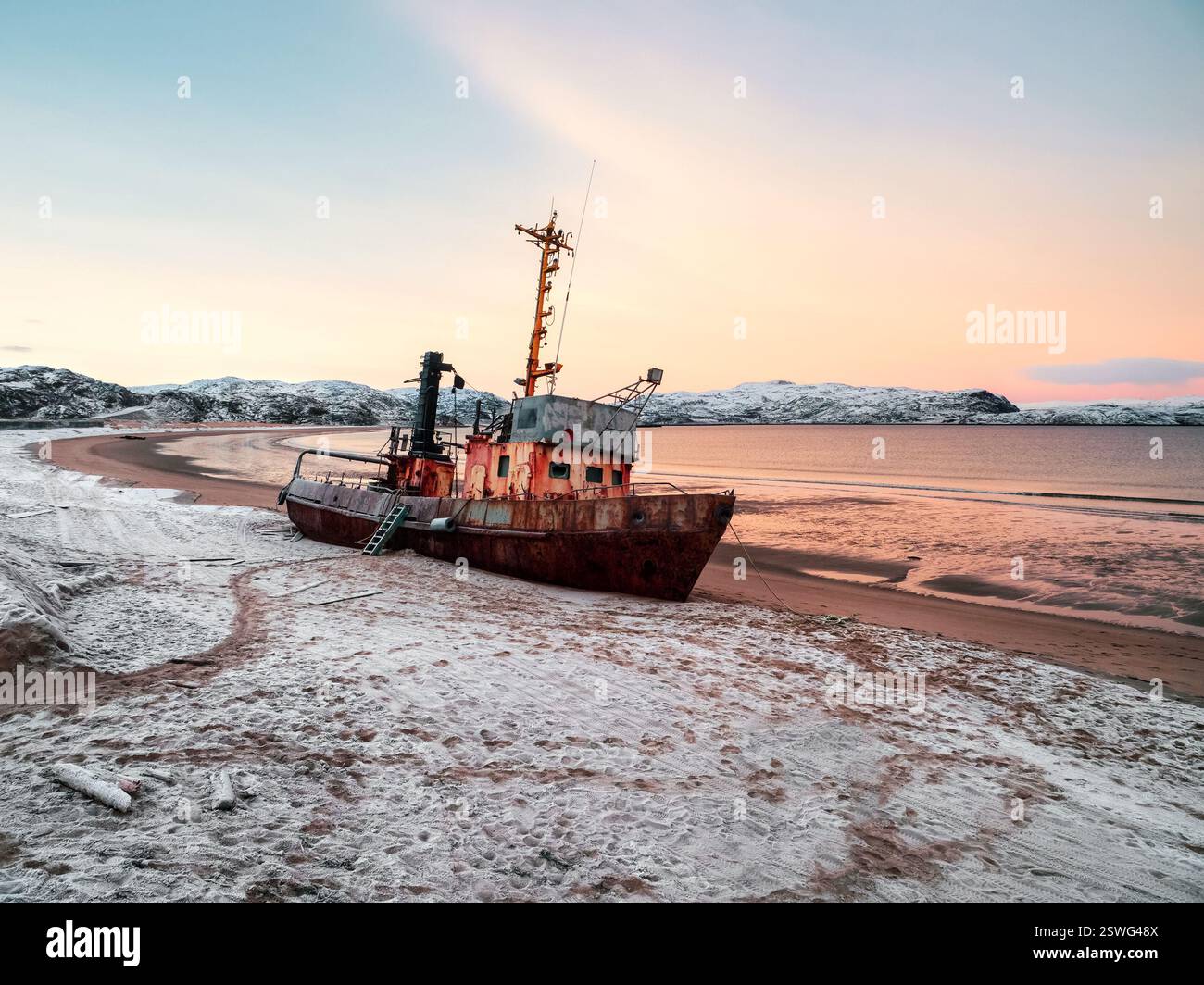 An old rusty fishing boat washed up on a sandy beach in the Barents Sea ...