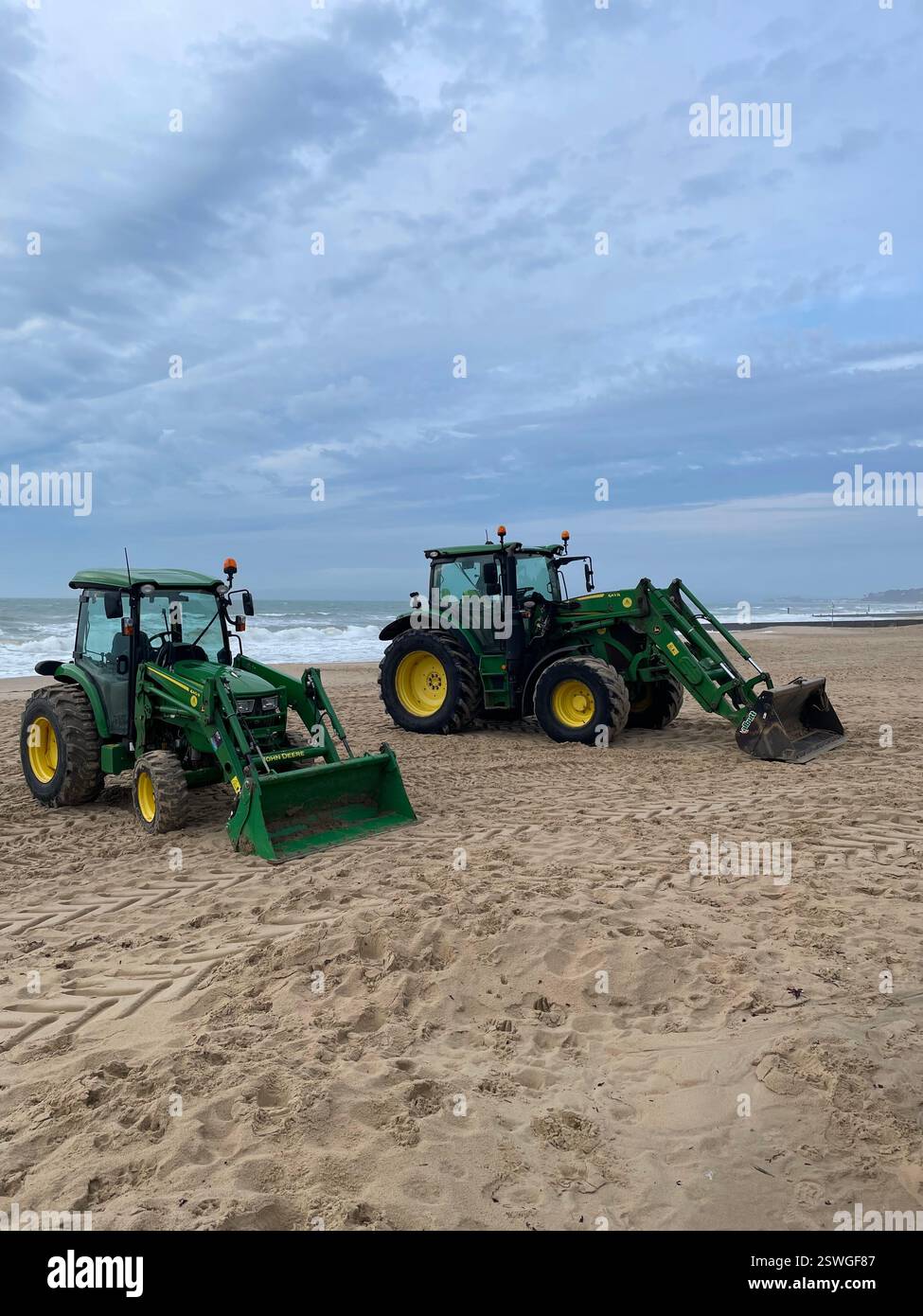 Two Green Tractors on Bournemouth Beach on a cloudy day in February. - Smartphone Captured Stock Image