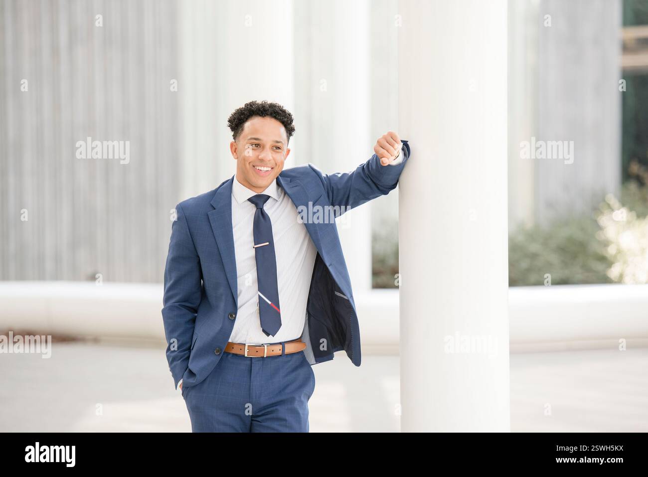 Business man smiling and leaning against pole Stock Photo