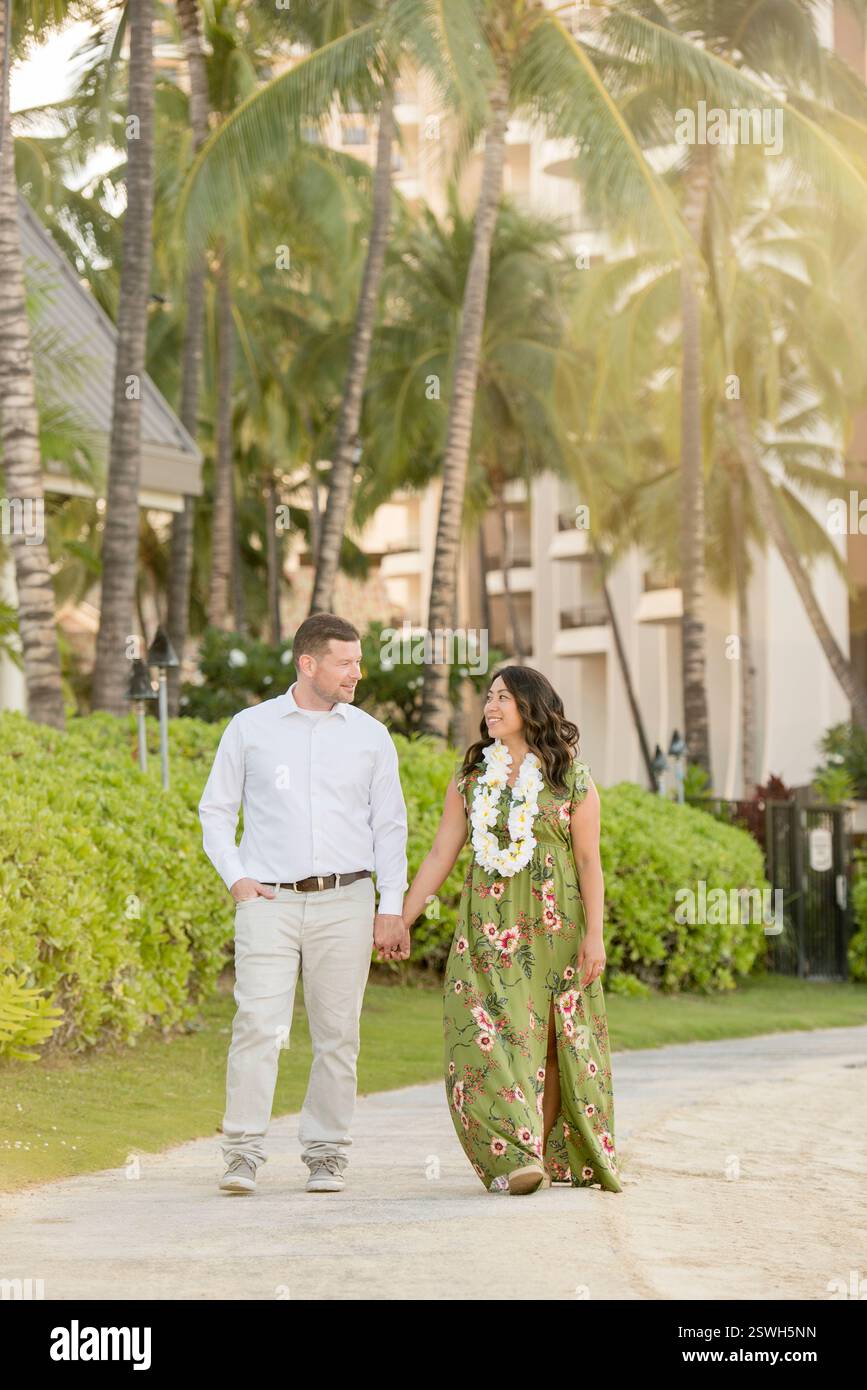 A couple strolls hand in hand through a tropical paradise at sunset ...