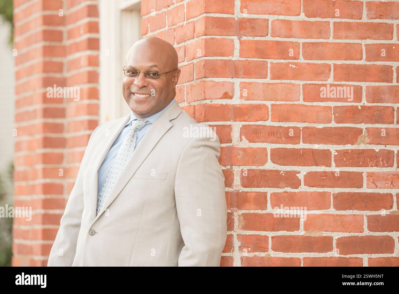 Stylish professional smiling warmly against a brick backdrop Stock Photo