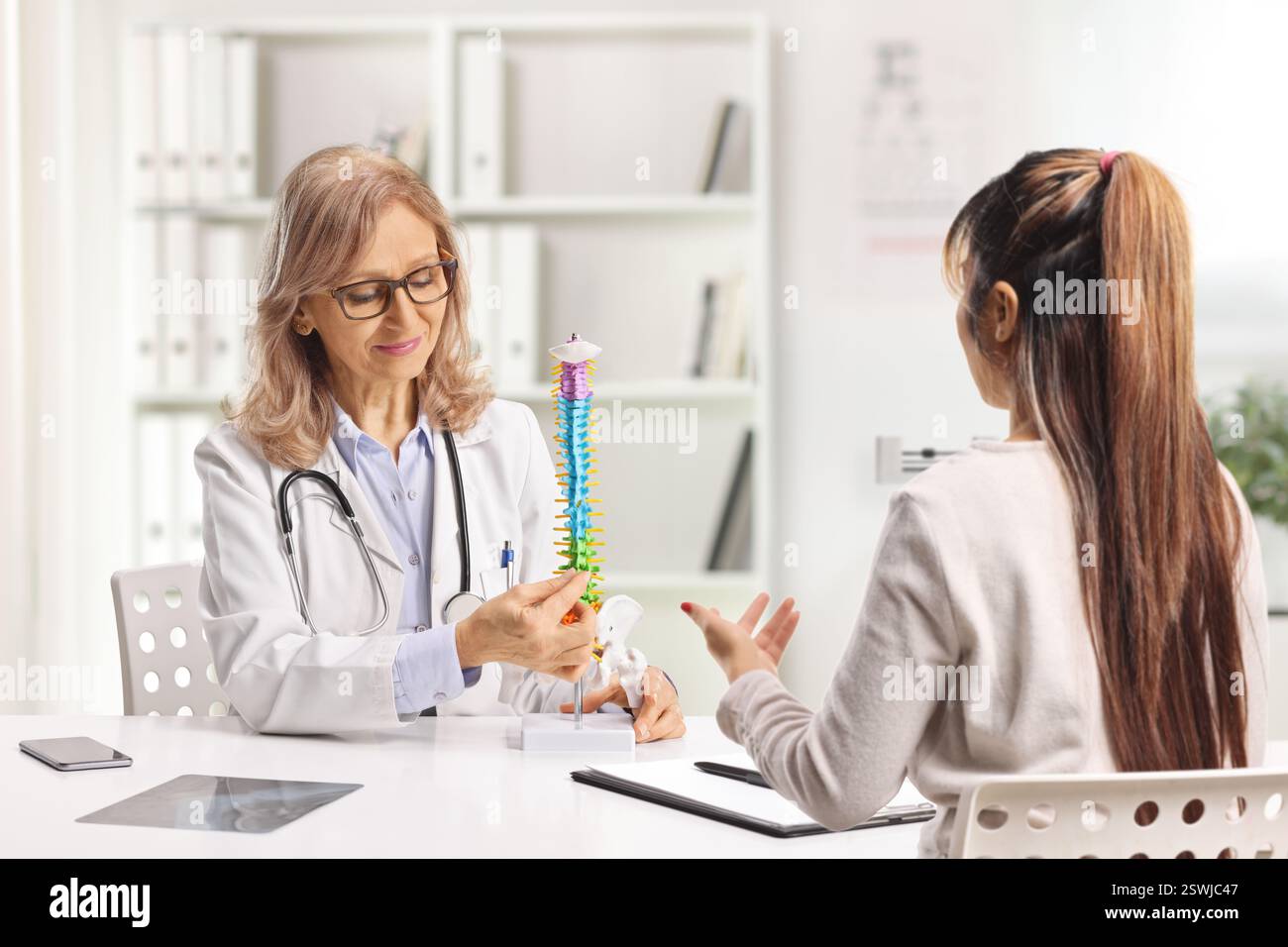 Woman at a hospital appointment with an orthopedic doctor looking at a human spine model Stock Photo