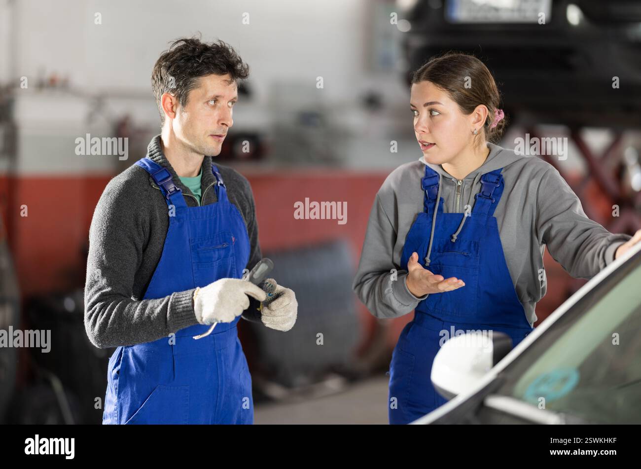 Two auto mechanics, man and woman, diagnosing a car engine together in ...