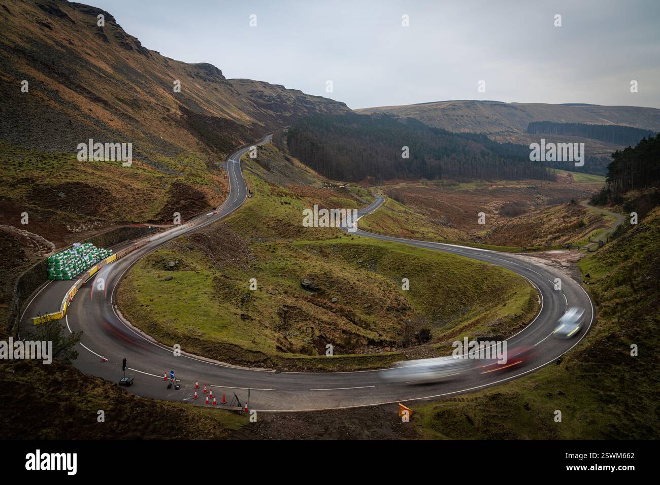 A winding road curves through a hilly landscape, with blurred cars ...
