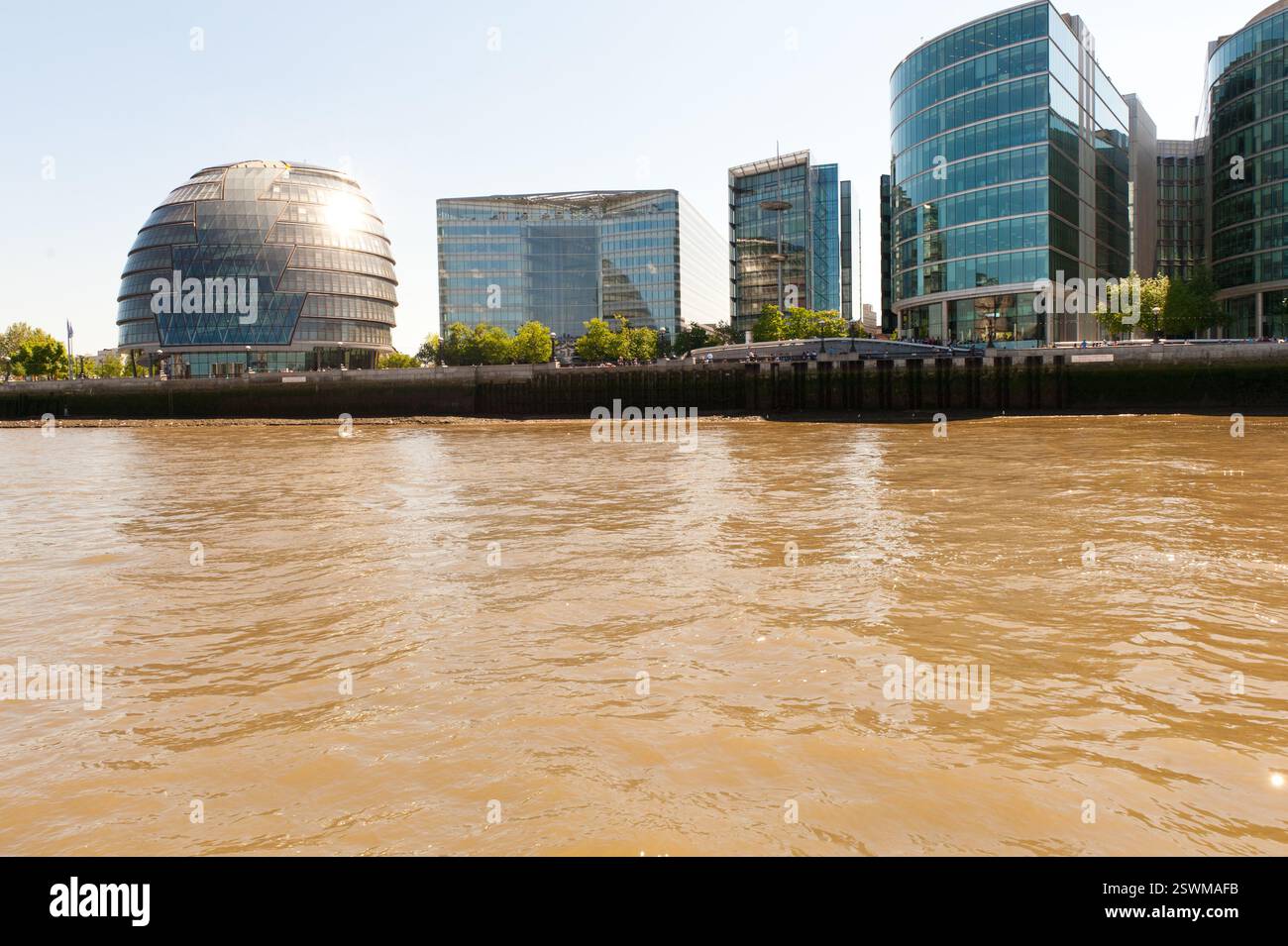The River Thames in London, England, shows the London City Hall and modern skyscrapers.  Water is discolored. Stock Photo