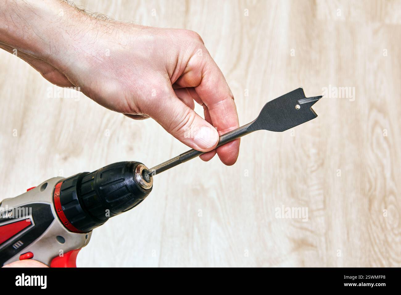 Cordless drill with spade bit held by hand. Stock Photo