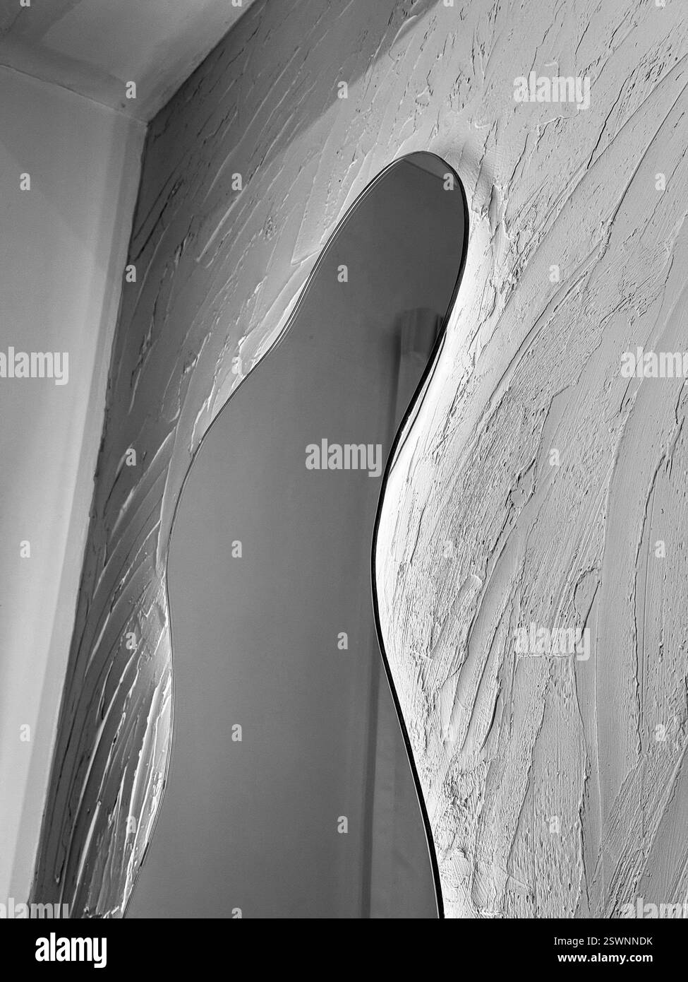 Black And White Mirror on Textured Wallace An organically shaped mirror with soft LED backlighting, mounted on a textured plaster wall. - Smartphone Captured Stock Image