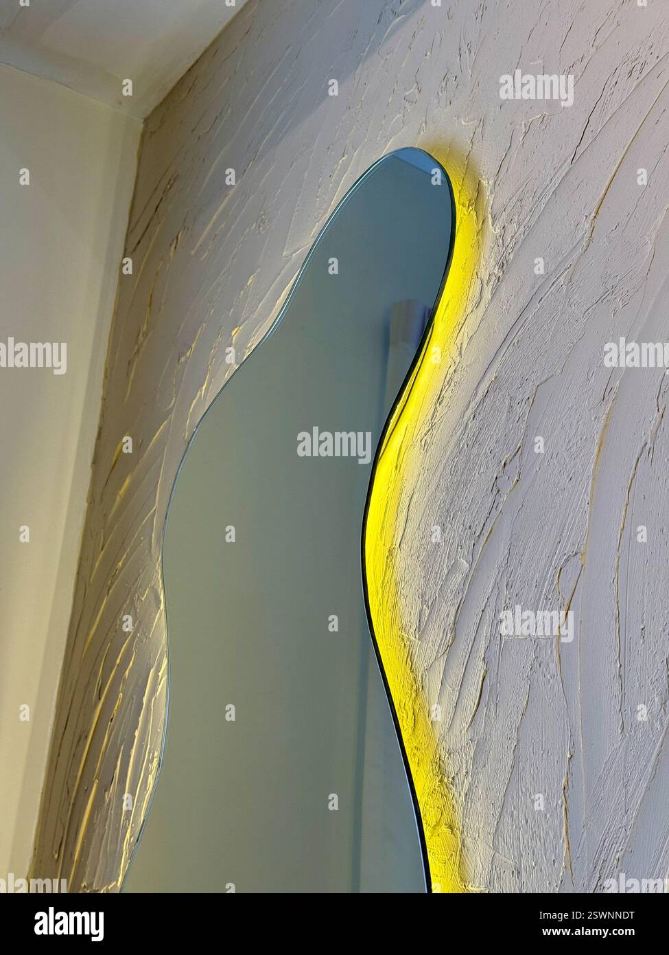 Organic Mirror with Warm Backlighting on Textured Wall An organically shaped mirror with soft yellow LED backlighting, mounted on a textured plaster - Smartphone Captured Stock Image