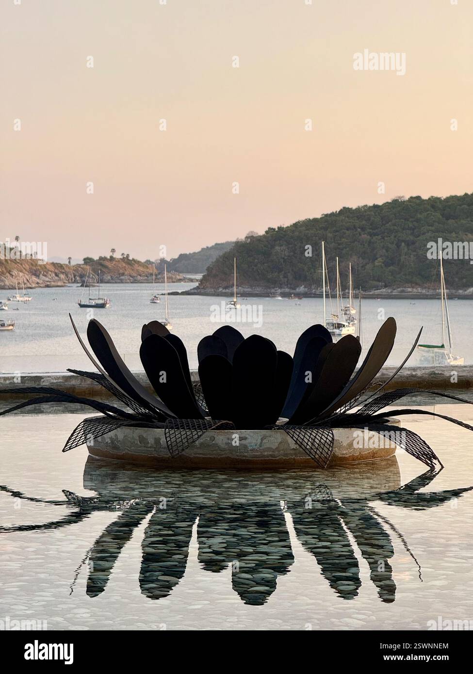 Floating Lotus Fire Pit Overlooking a Tropical Bay A metal fire pit shaped like a lotus flower floats on a calm water basin, with flames glowing - Smartphone Captured Stock Image