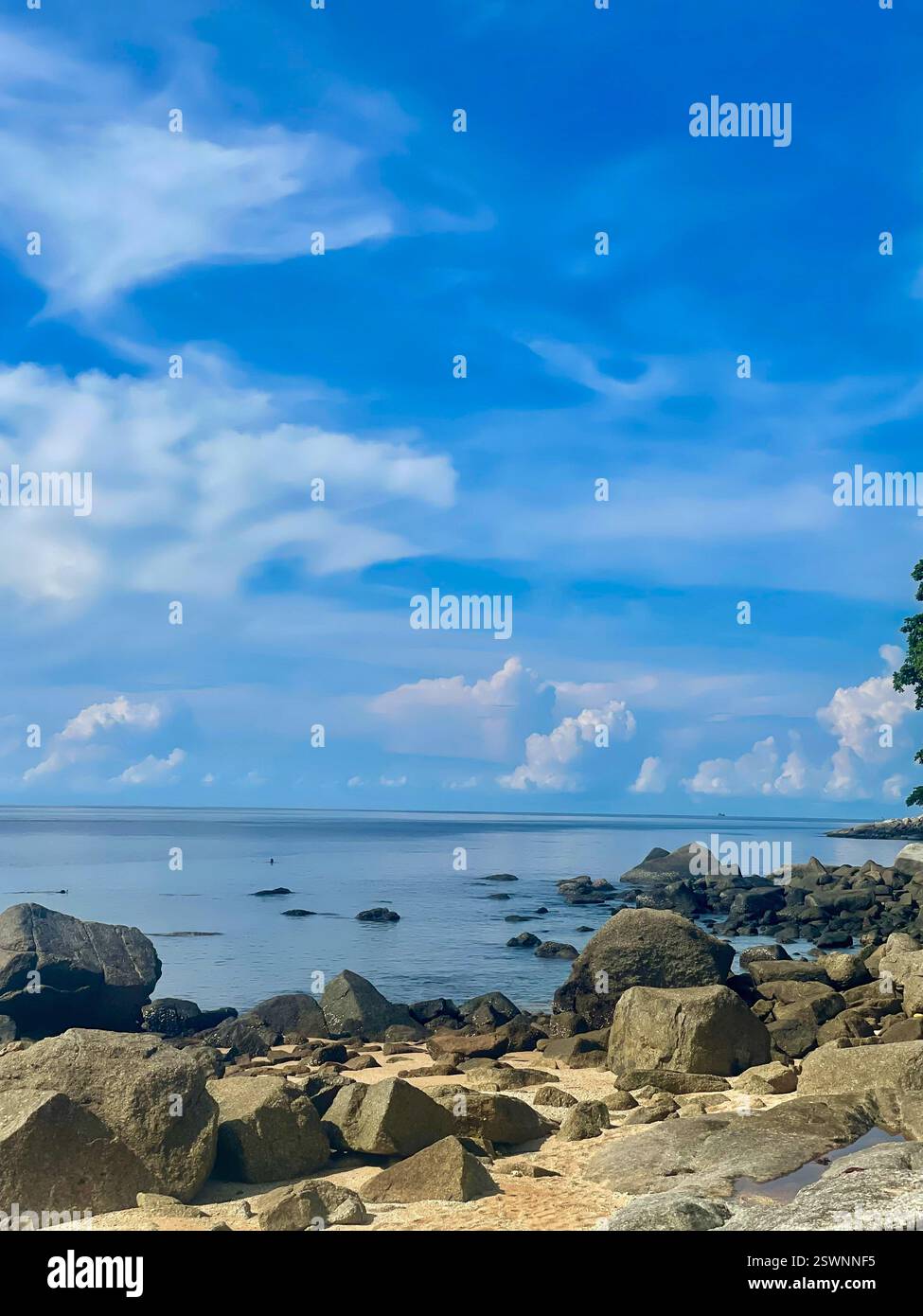 Rocky Coastline and Calm Sea A rocky coastline meets a calm sea under a blue sky with scattered clouds. - Smartphone Captured Stock Image