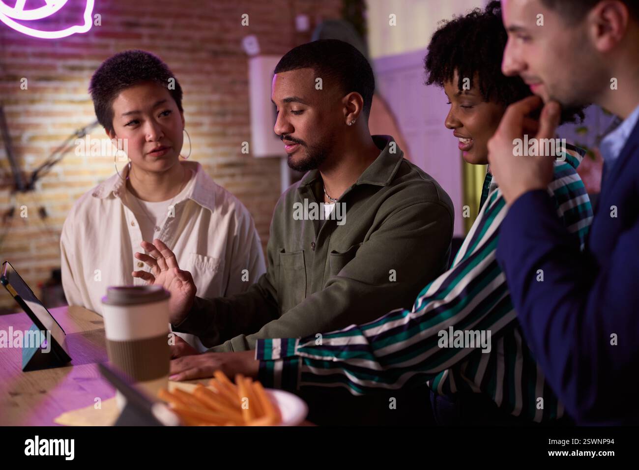 Diverse business team collaborating on a project using tablet in modern office space Stock Photo