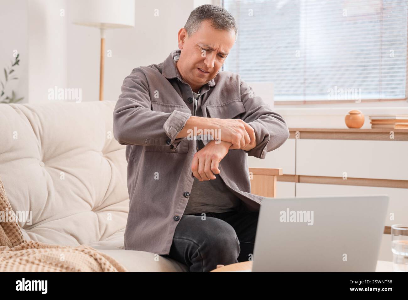 Mature man suffering from wrist pain on sofa at home Stock Photo - Alamy