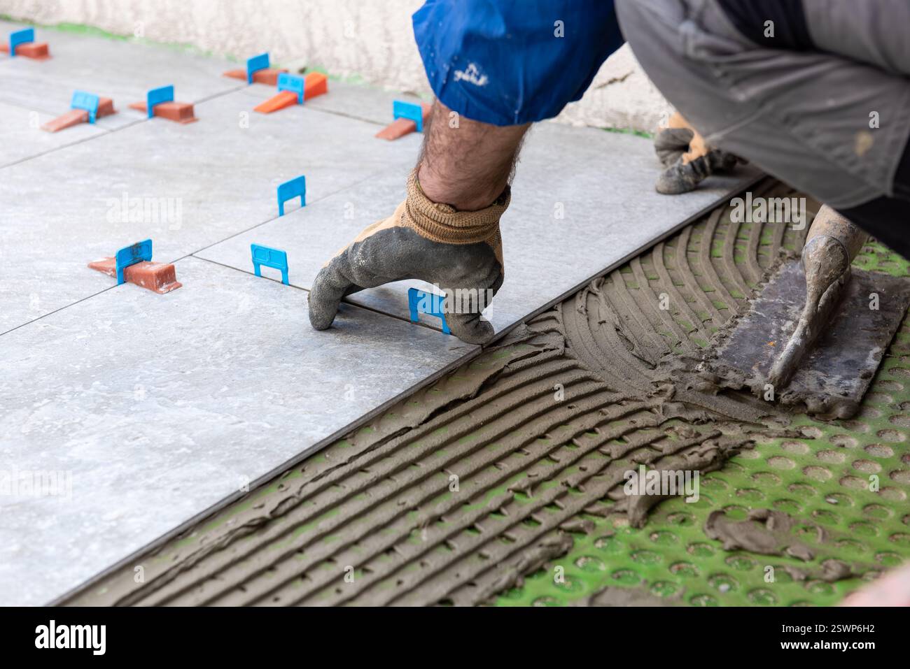 Bricklayer tiler installs tiles using leveling spacers. Construction industry. Building. Stock Photo