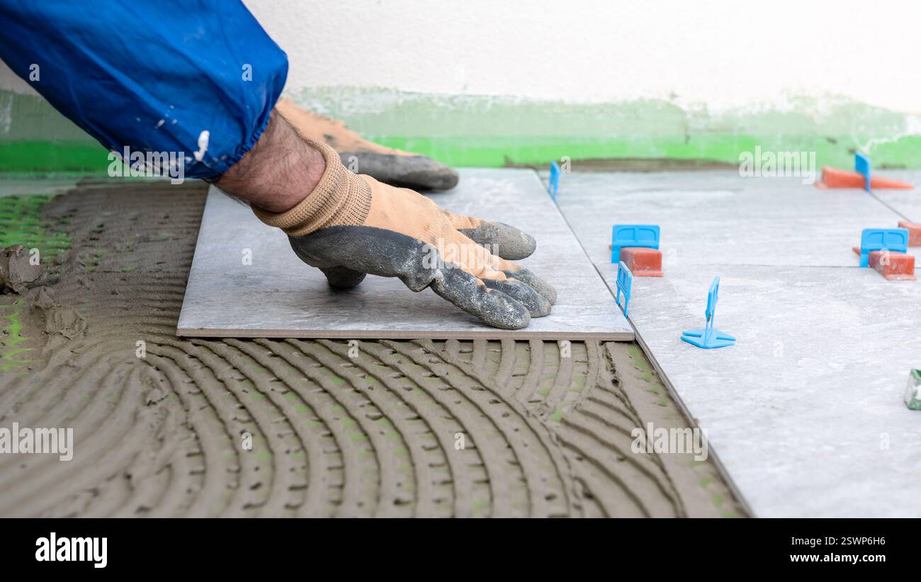 Bricklayer tiler installs tiles using leveling spacers. Construction industry. Building. Stock Photo