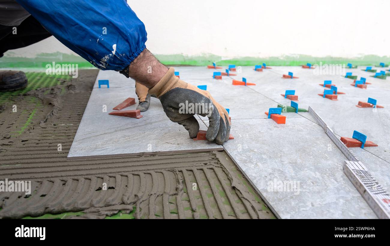 Bricklayer tiler installs tiles using leveling spacers. Construction industry. Building. Stock Photo