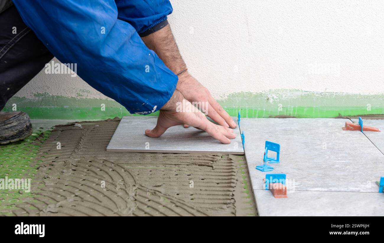 Bricklayer tiler installs tiles using leveling spacers. Construction industry. Building. Stock Photo