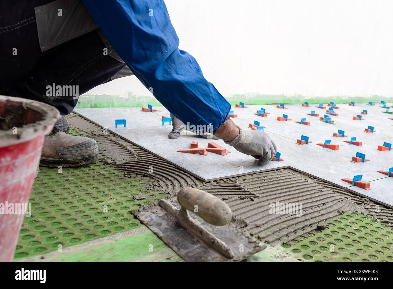 Bricklayer tiler installs tiles using leveling spacers. Construction industry. Building. Stock Photo