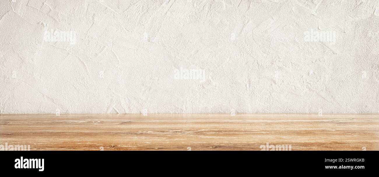 Rustic wooden table surface with a textured white wall background in a well-lit kitchen. Stock Photo