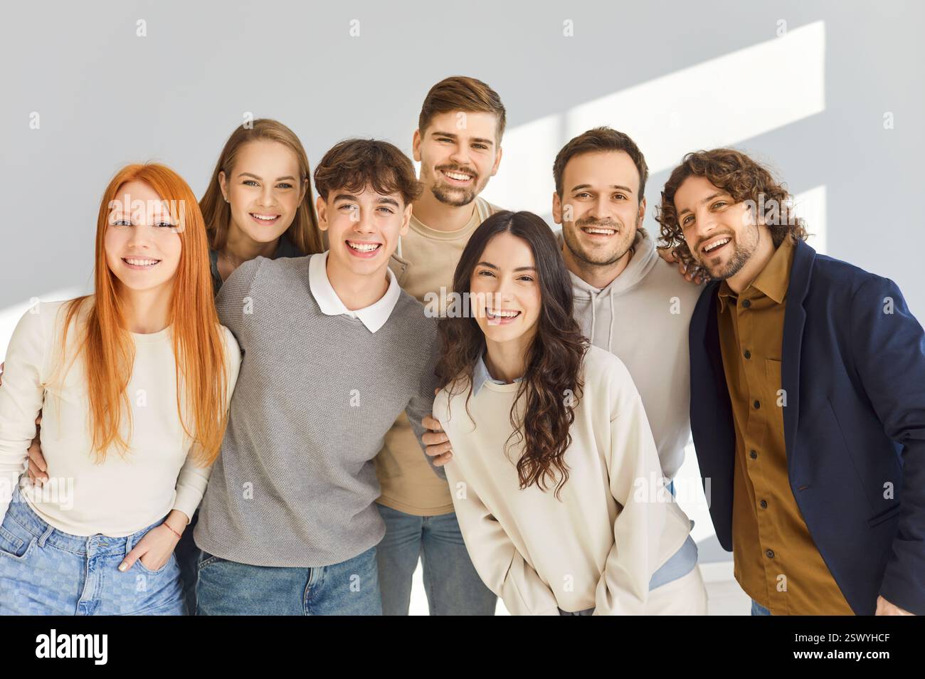 Happy young friends standing together, smiling at camera, hugging each ...