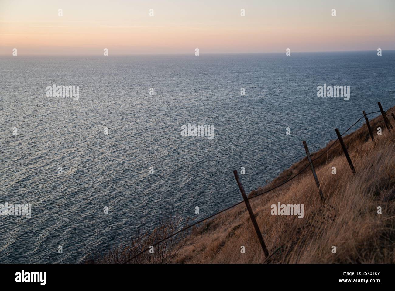 Old fence stretching across barren patterned dry field, sea and sunset ...