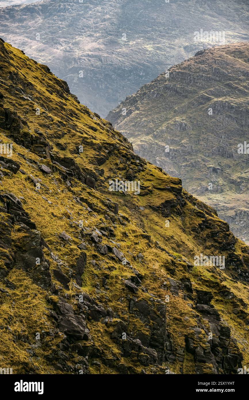 Rugged mountains rise sharply, displaying steep grassy slopes and rocky ...