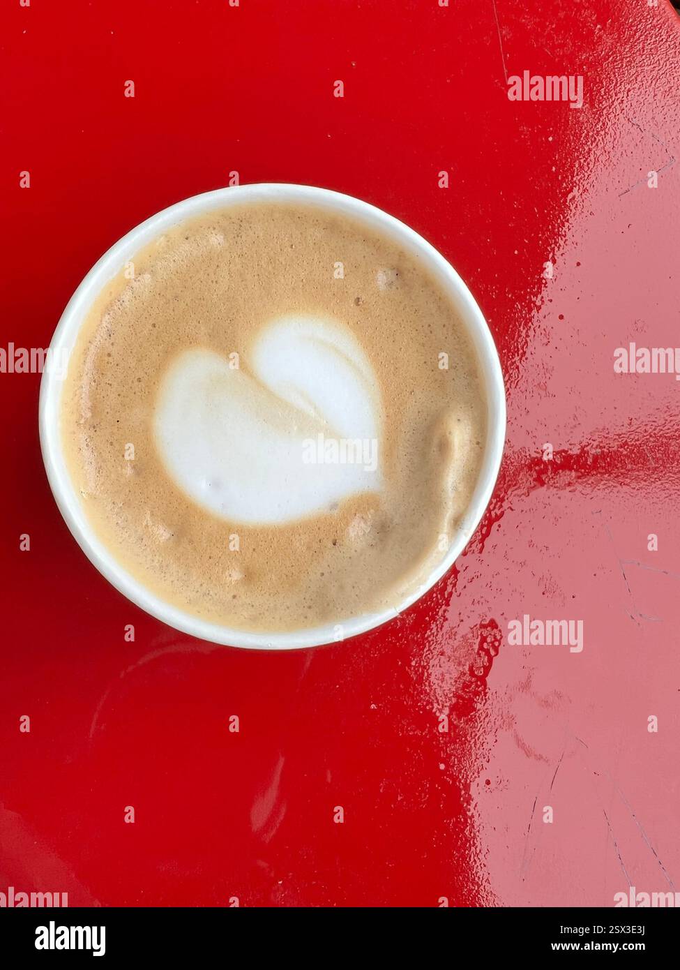 Cup of cappuccino with heart-shaped latte art on a red table - Smartphone Captured Stock Image