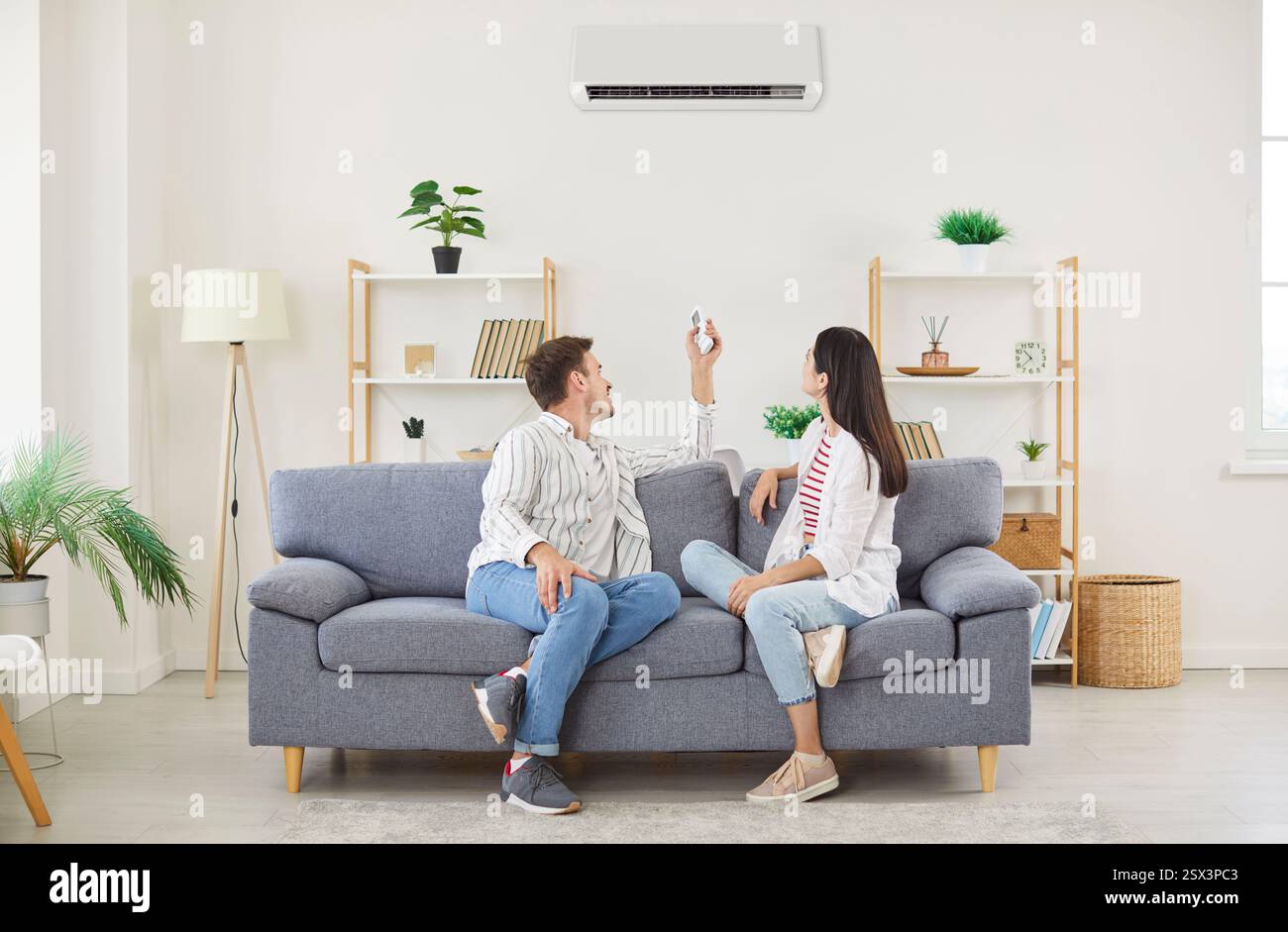 Climate control couple air conditioner fixing sitting relaxing on sofa holding controller, regulate  Stock Photo