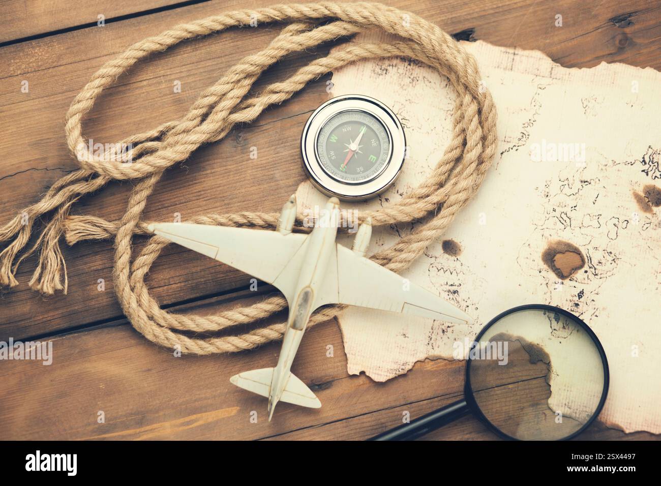 airplane, old map, compass with magnifier on wooden table Stock Photo