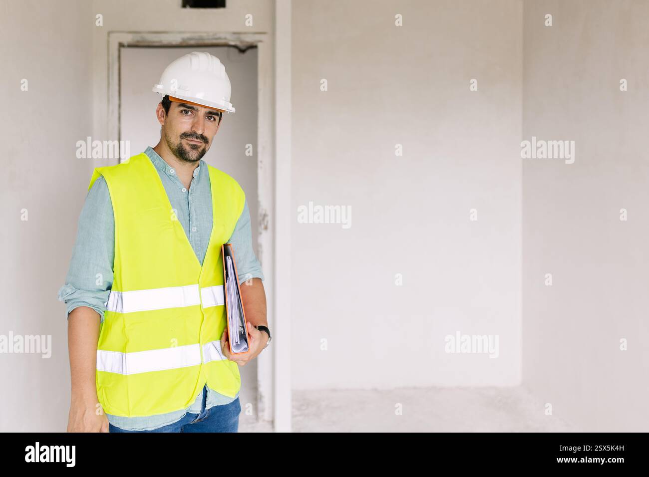 Construction engineer wearing safety vest and holding folder is ...