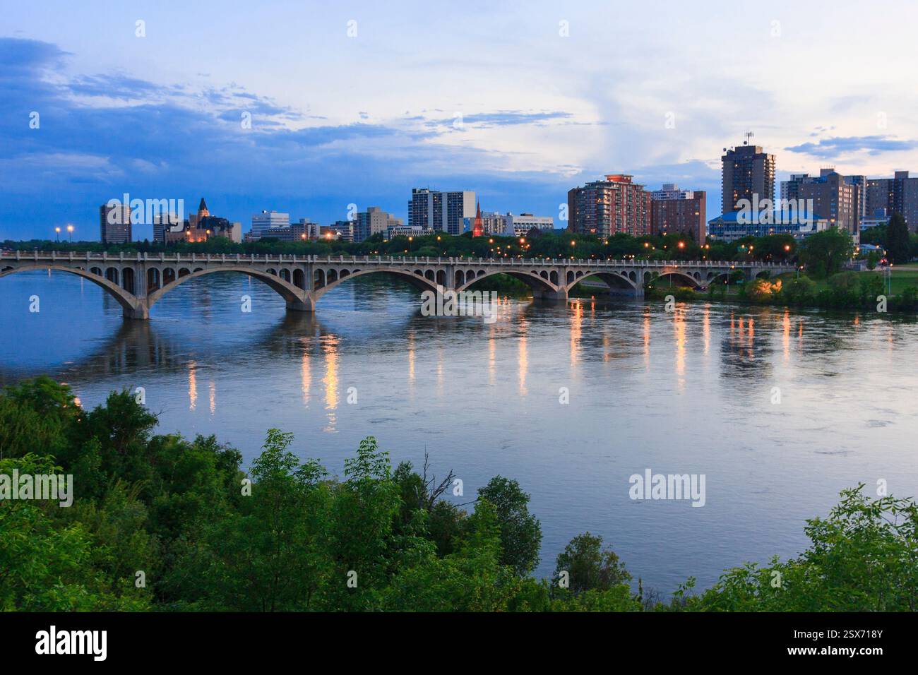 City view of a bridge over a river with a city skyline in the background. The bridge is lit up at night, creating a serene and peaceful atmosphere Stock Photo