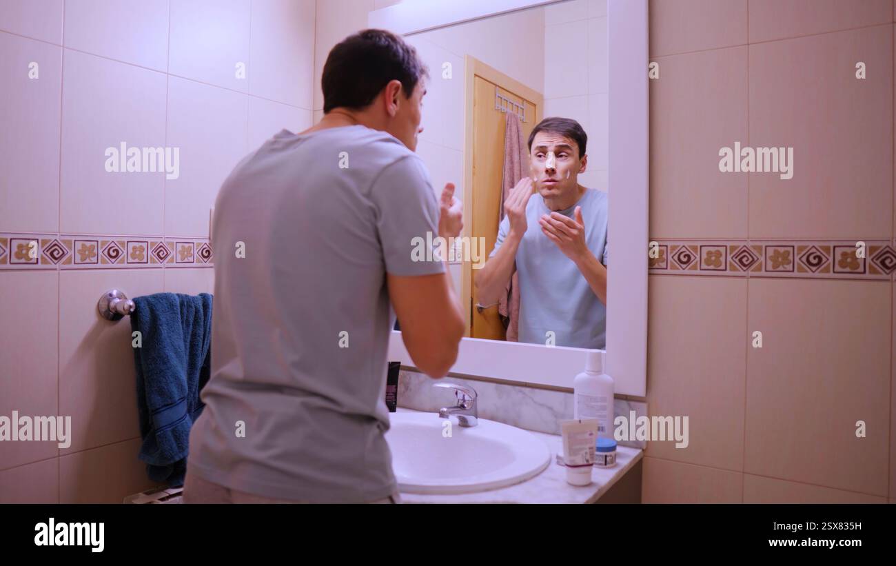 Man applying face cream in bathroom mirror Stock Photo