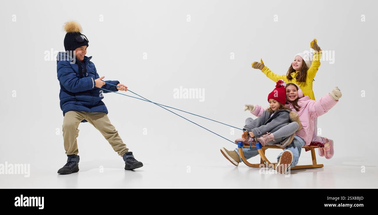 Boy pulling sled with three girls sitting, all dressed in cozy winter ...