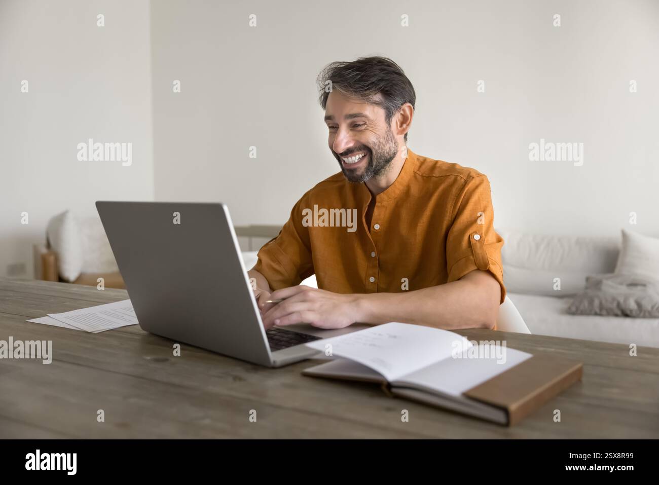 Happy middle-aged man sitting at table using laptop Stock Photo