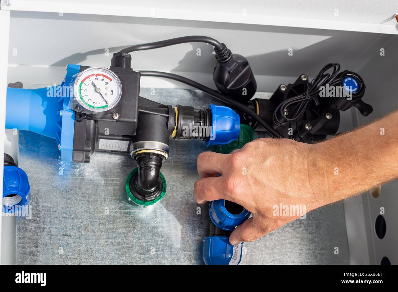 A man installs a drip irrigation system by placing a polypropylene compression tee into a metal box. Stock Photo