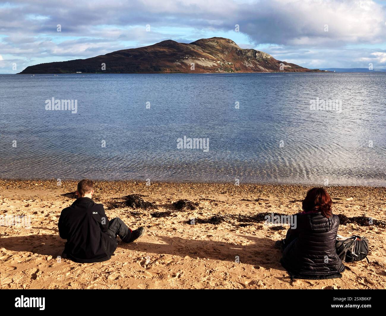Sitting on the beach with a view towards Holy Isle from Lamlash bay, Isle of Arran, Firth of Clyde, Scotland - Smartphone Captured Stock Image