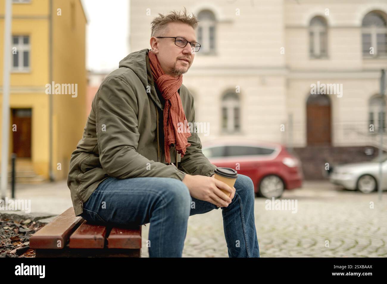 Young Attractive Man Sits On Park Bench Drinking Coffee And Waiting Stock Photo