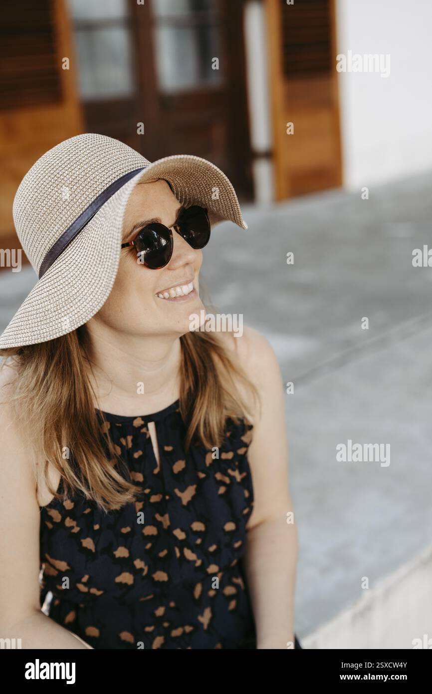 Woman with sunglasses and sun hat sitting on stone steps Stock Photo