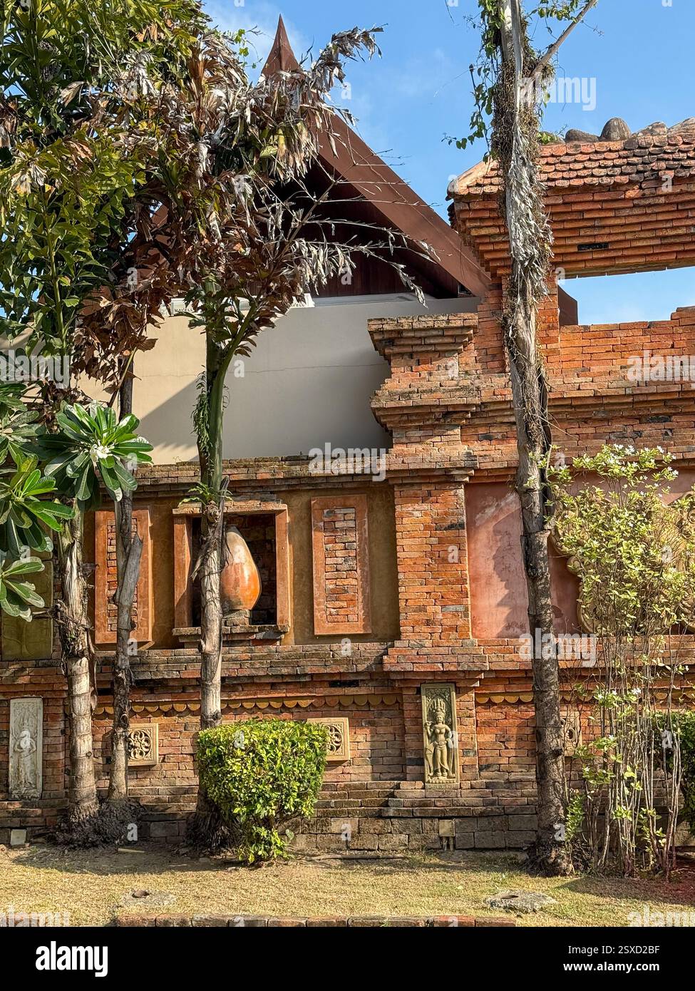Red Brick Wall with Traditional Sculptures and Tropical Vegetation A red brick wall adorned with traditional sculptures and decorative motifs, partial - Smartphone Captured Stock Image