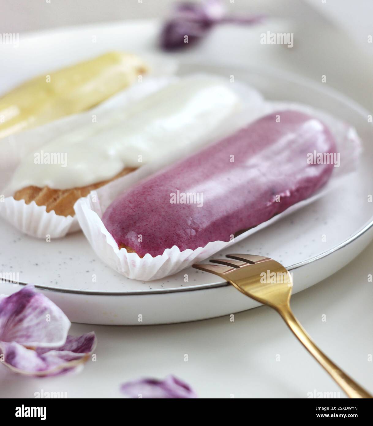 Three eclairs with different fillings lie in a plate on the table Stock Photo