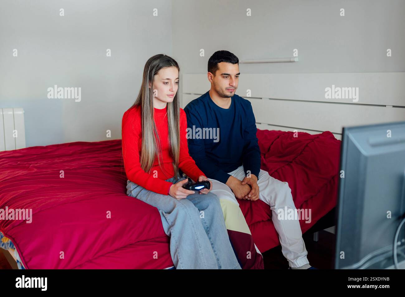 Young couple playing video games in bedroom using wireless controller Stock Photo