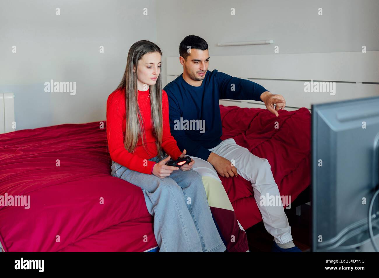 Young couple playing video games in bedroom using wireless controller Stock Photo