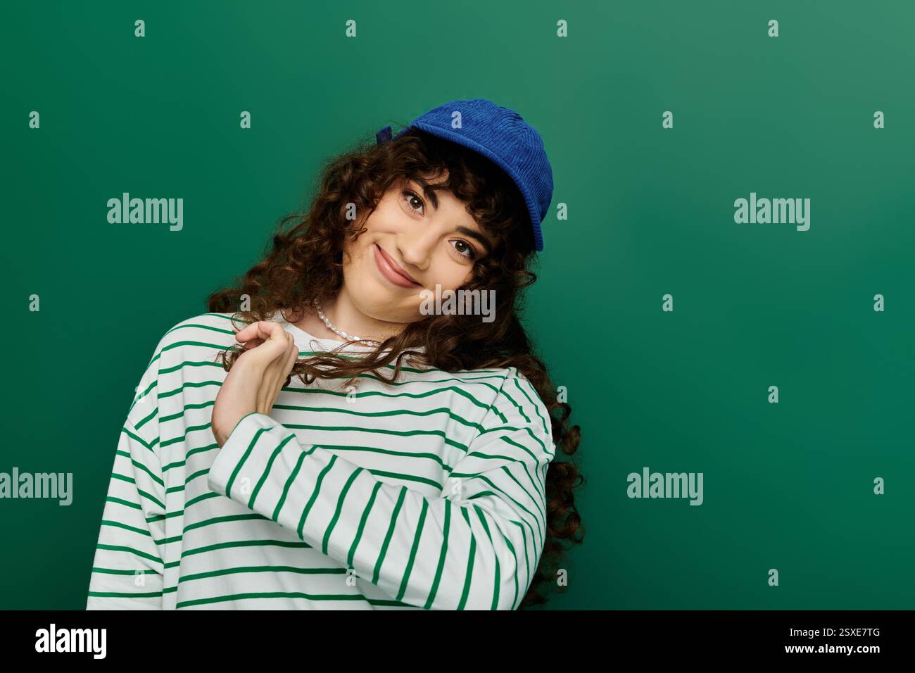 A young woman with curly hair expresses joy while posing against a ...