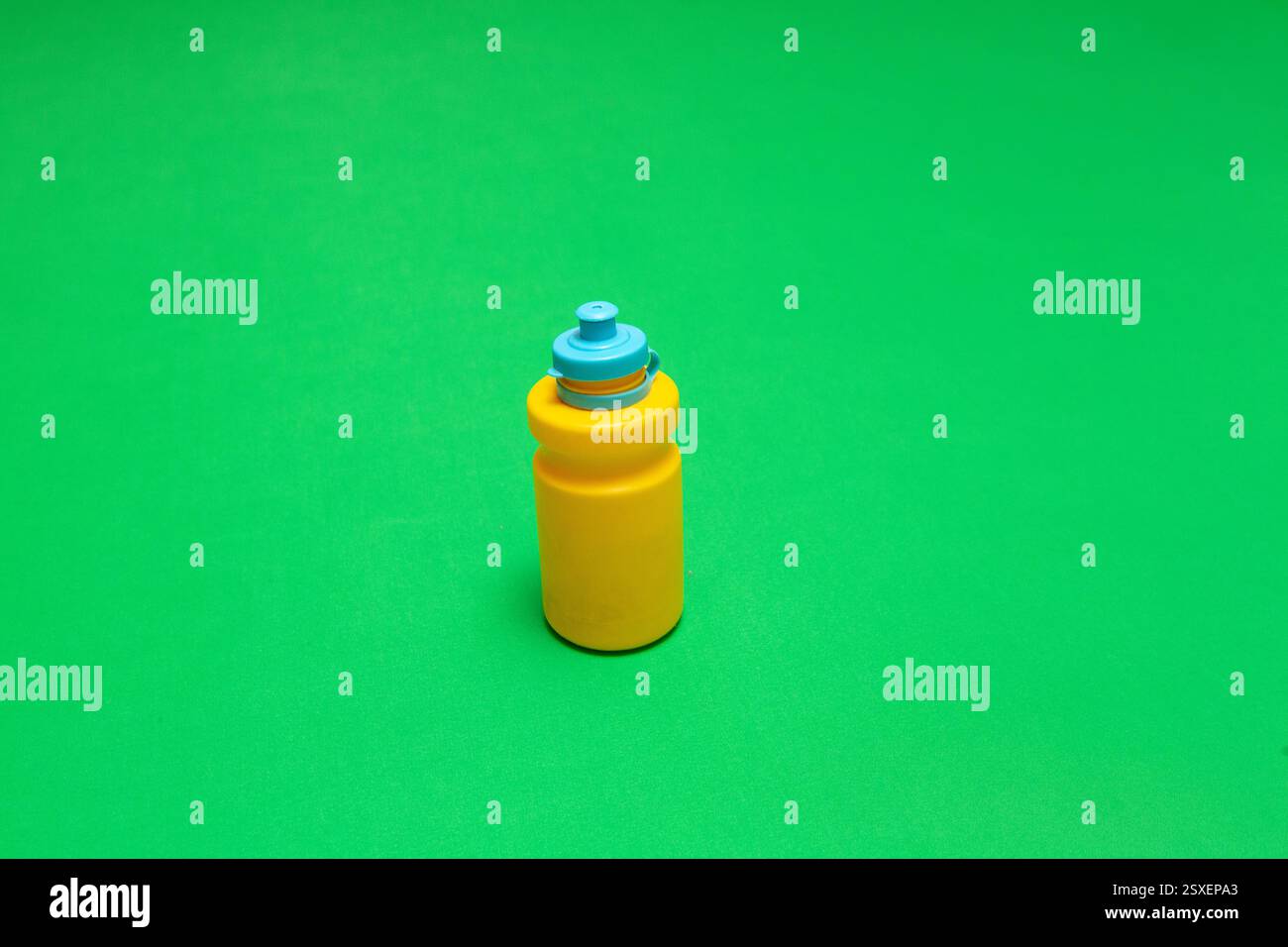 Yellow plastic water bottle with blue cap on green background, promoting hydration and an active lifestyle Stock Photo