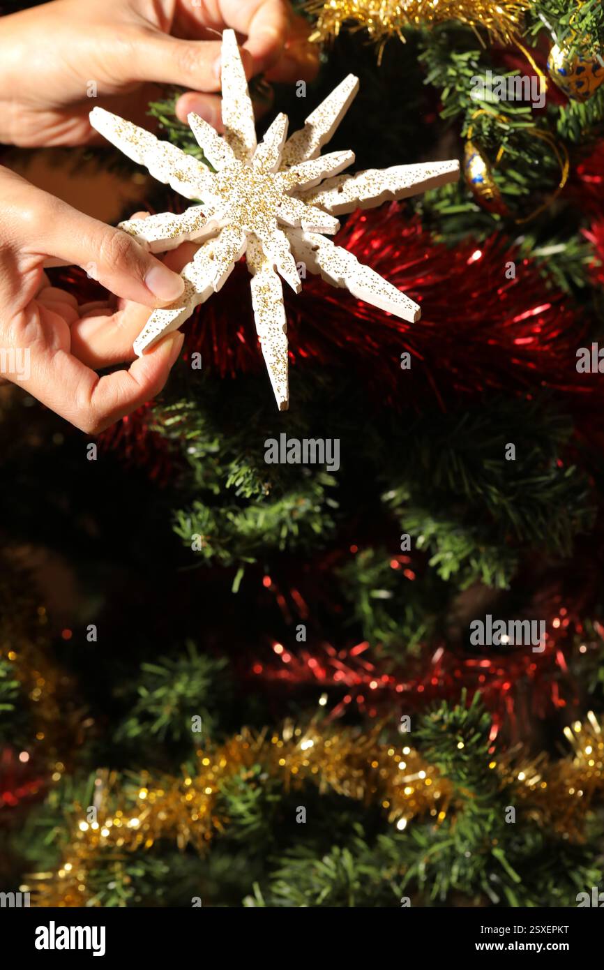 Hands decorating christmas tree with white wooden snowflake and gold glitter, festive holiday season Stock Photo