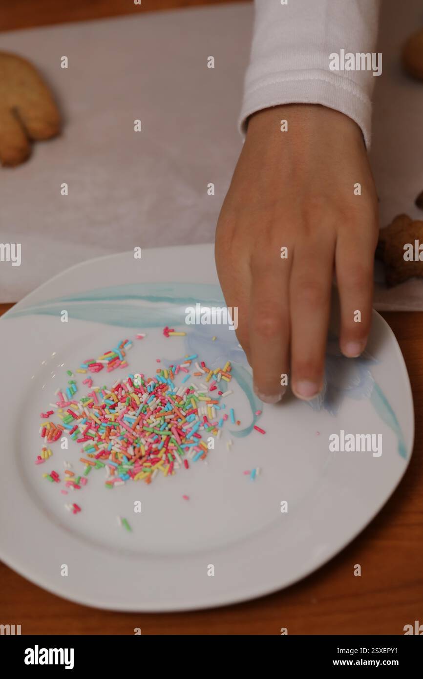 Kid gathering colorful sprinkles from a plate while preparing cookies ...