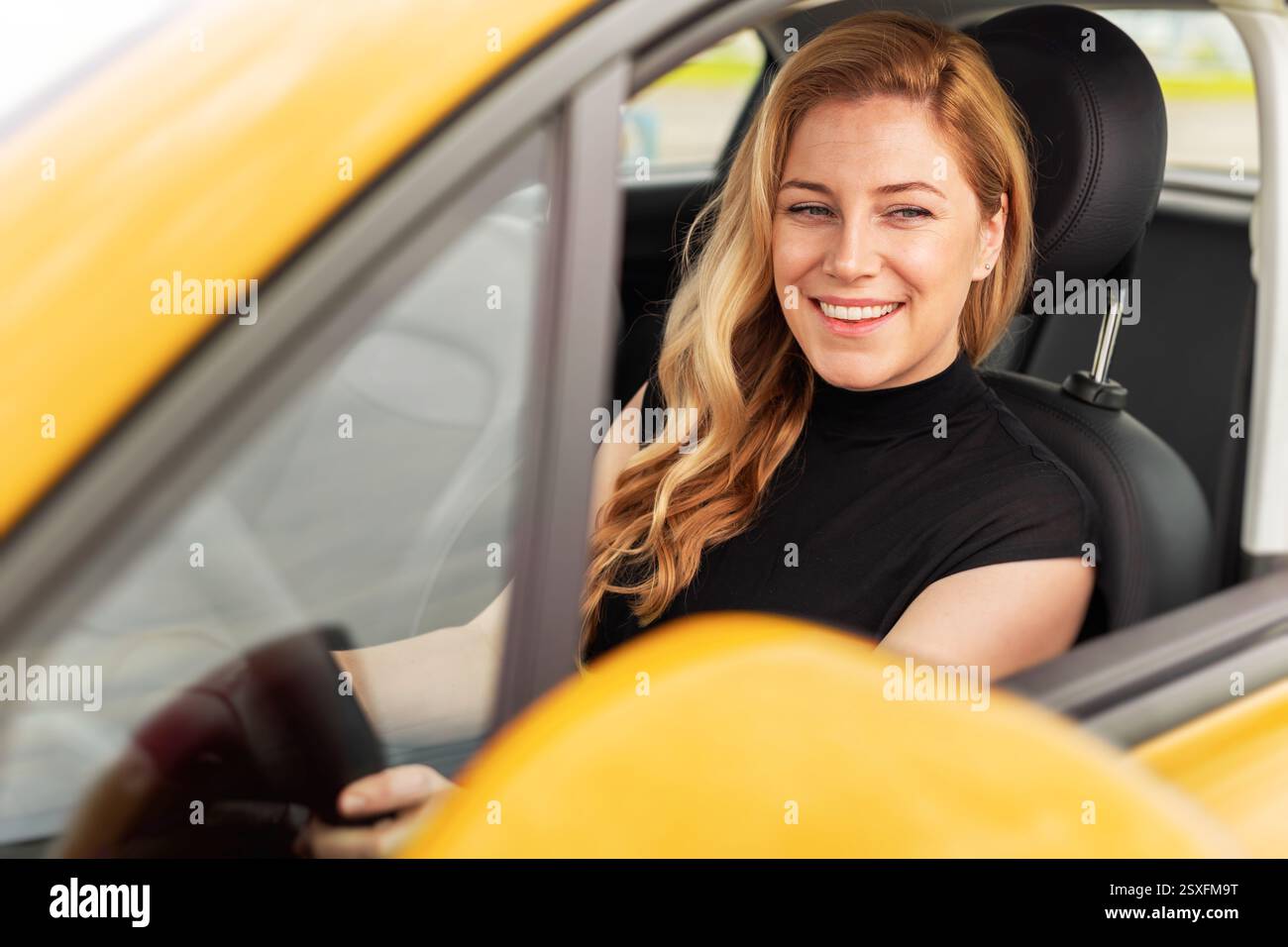 A smiling blonde woman sits in the driver's seat of a yellow car ...
