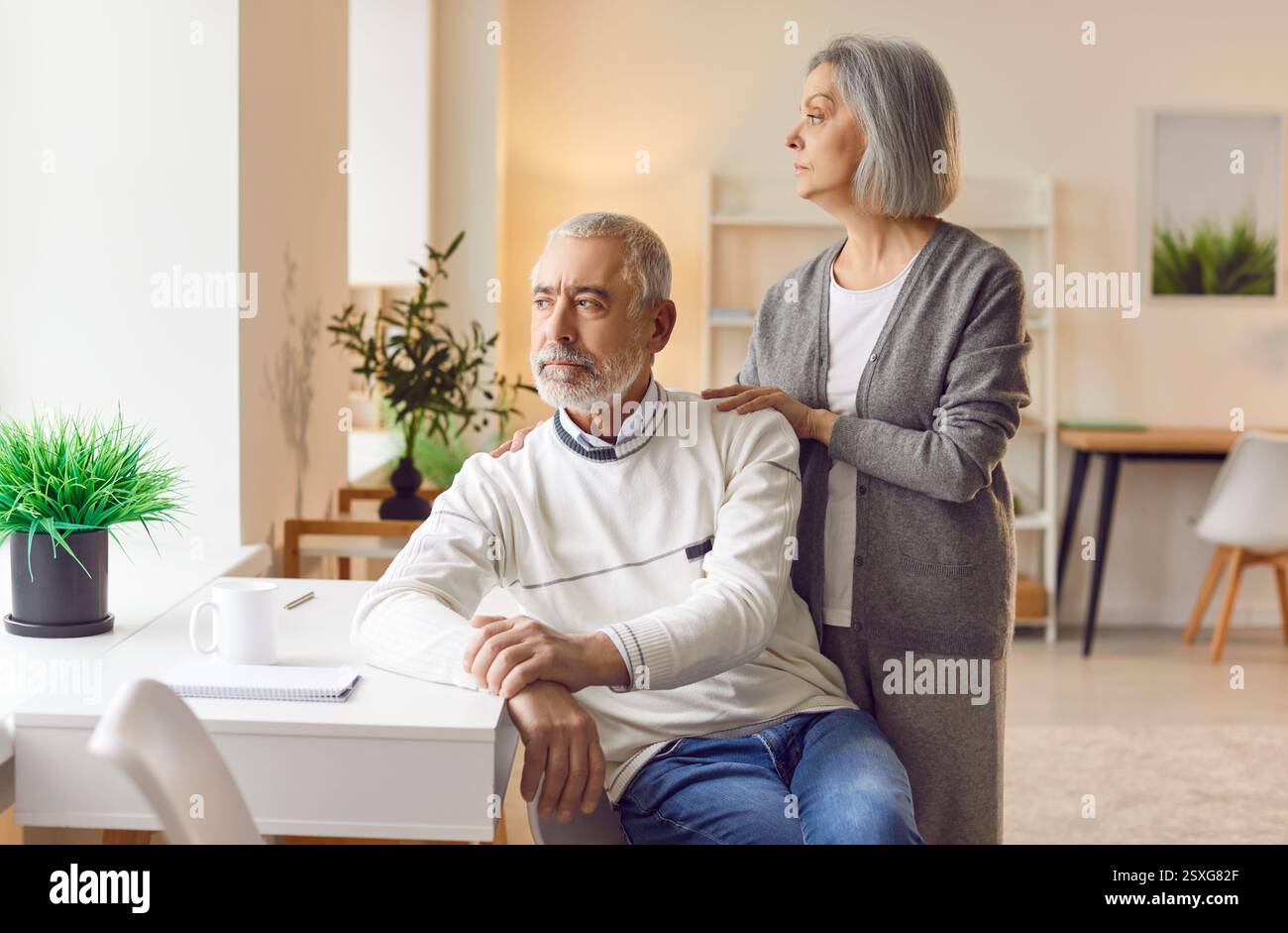 Thoughtful senior couple contemplating decision while looking into distance through window. Stock Photo