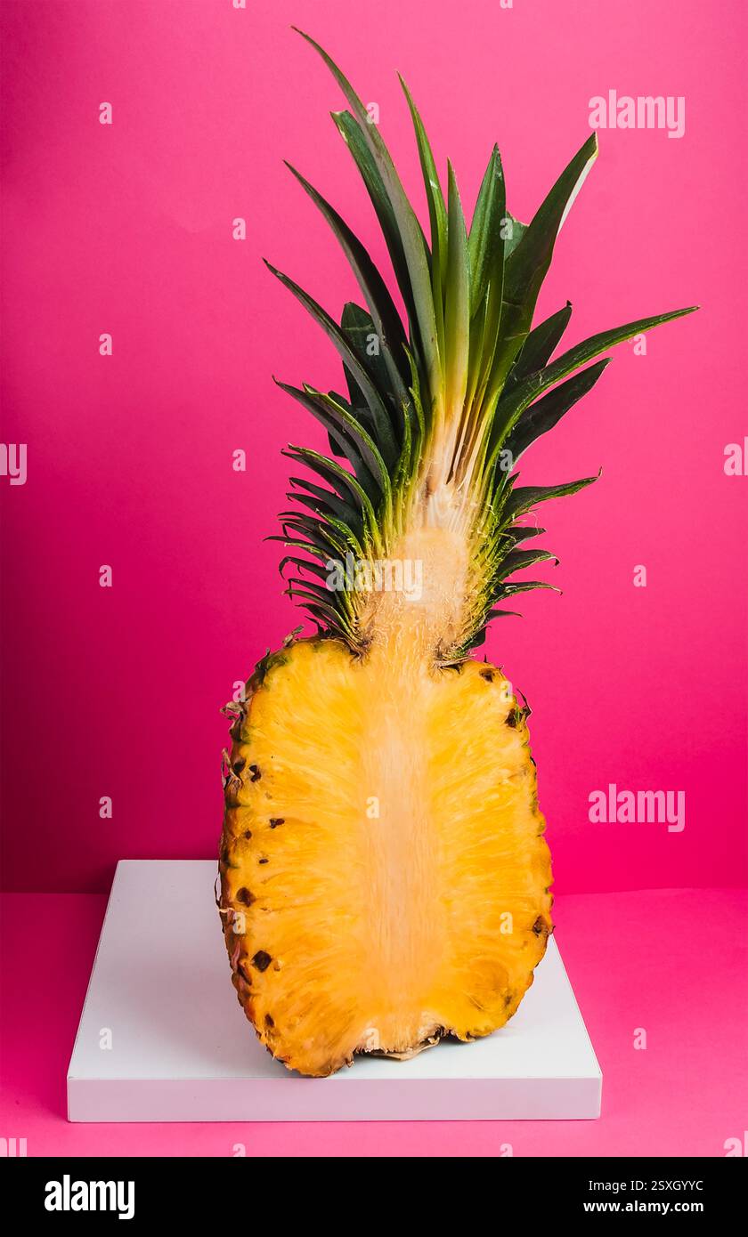 This pineapple, sliced in half, reveals its juicy yellow flesh and detailed texture, set against a bold pink backdrop for a striking visual contrast. Stock Photo