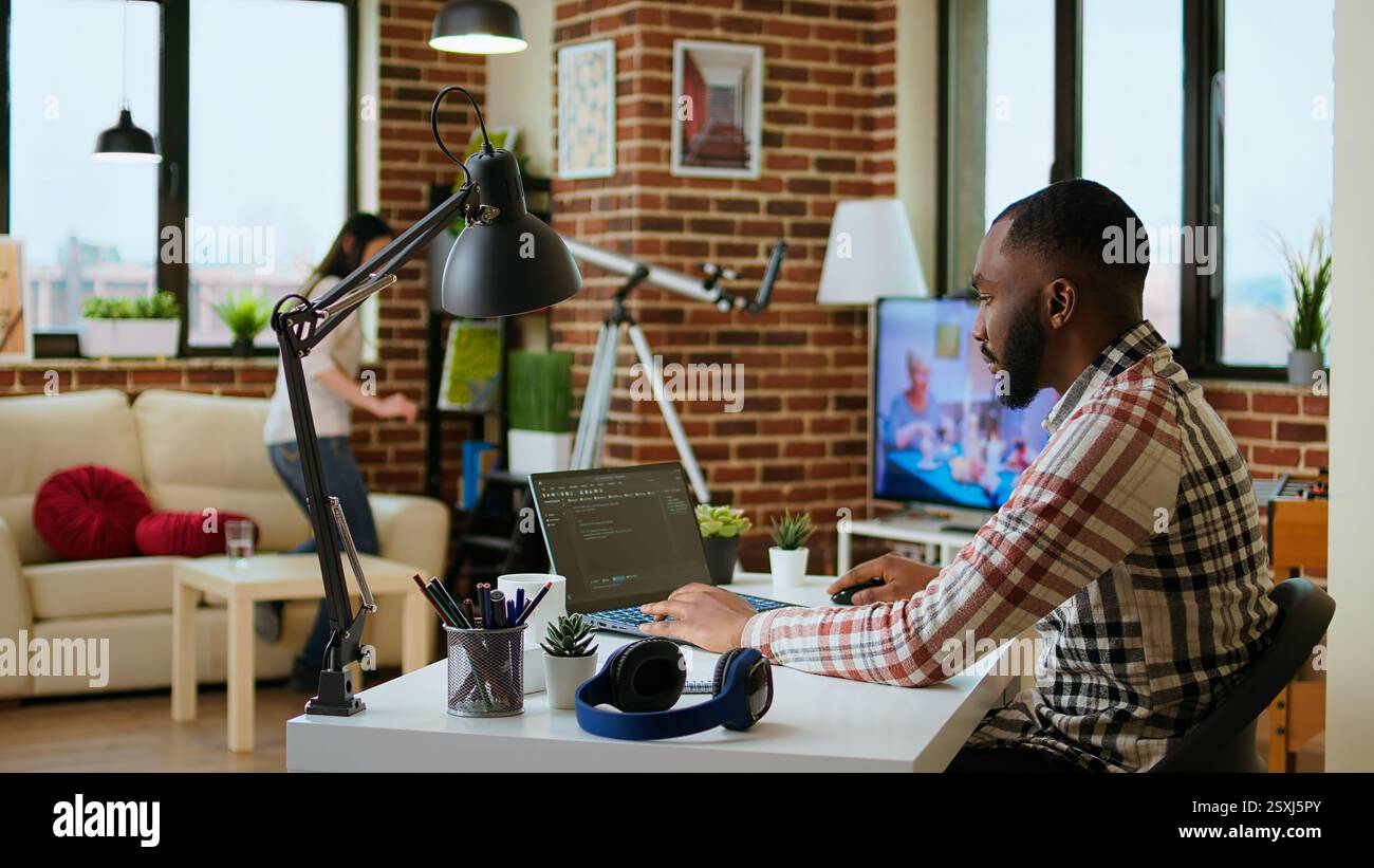 African american software developer works on programming code on a laptop in remote workspace. Productive IT engineer working on coding, software design and internet security innovation. Camera A. Stock Photo